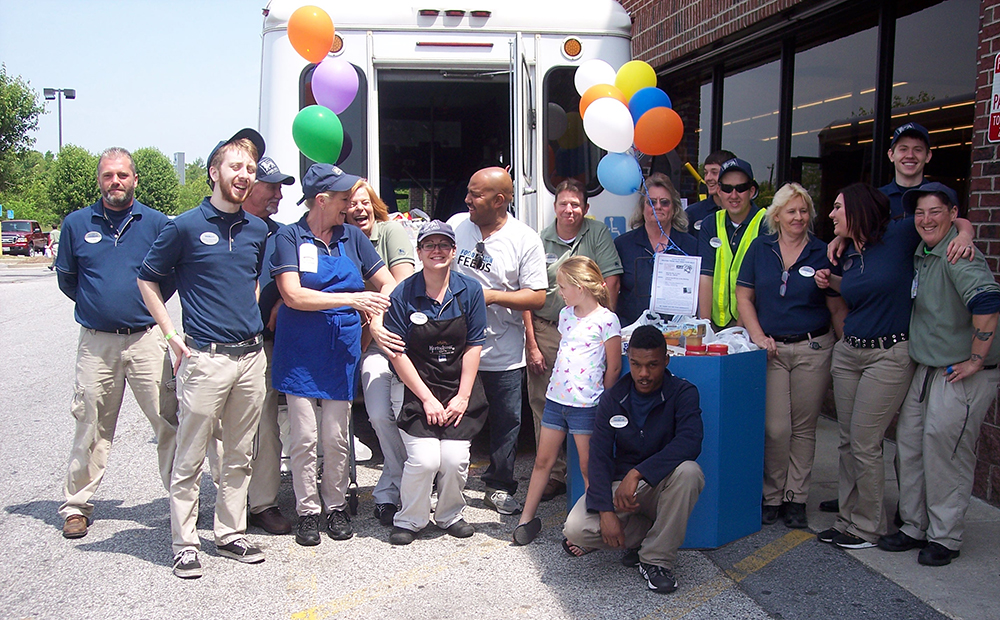 A group of 17 Stuff the Bus volunteers standing in front of a bus.